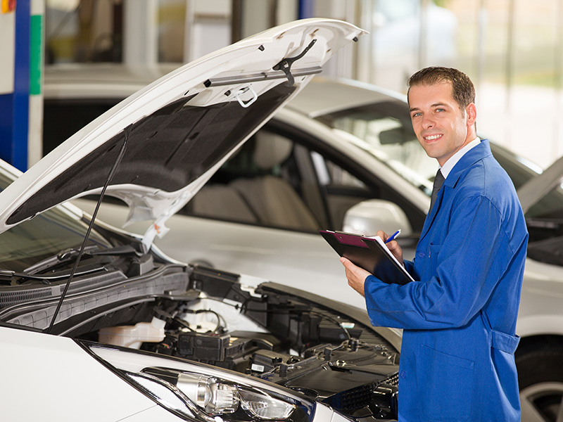 Volkswagen service technician inspecting a car engine with the hood open at a dealership service center.