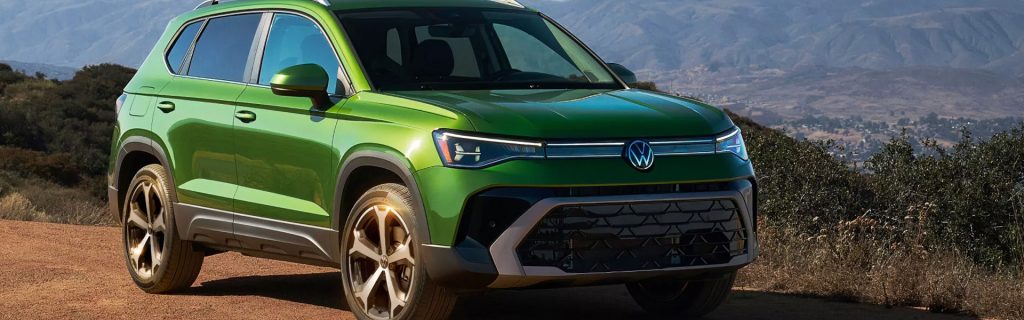 Green 2026 Volkswagen Taos compact SUV parked on a scenic hillside with mountains in the background.