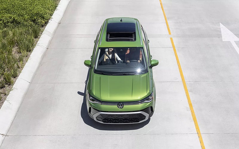 Green Volkswagen SUV with panoramic sunroof driving on a road.