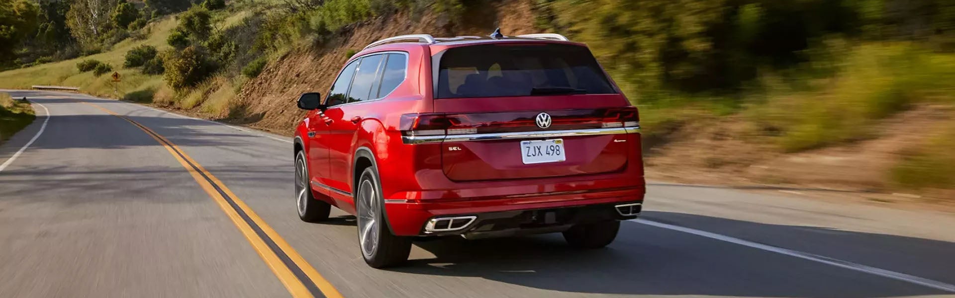 Red Volkswagen Atlas SUV driving on a winding countryside road.