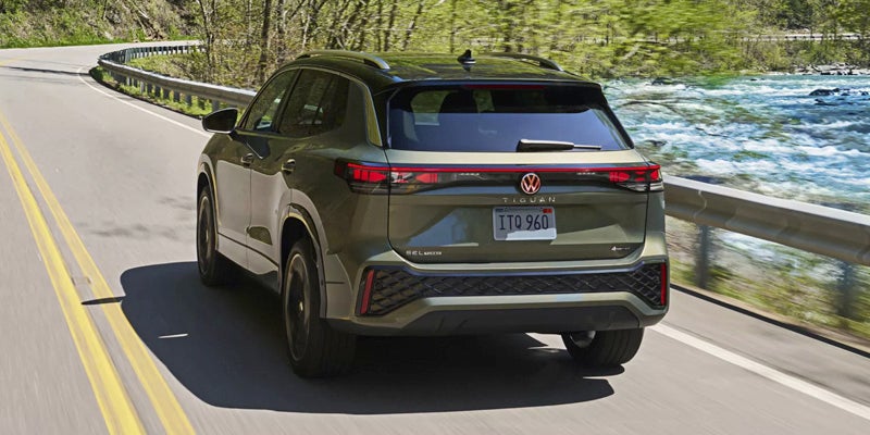 Rear view of the 2026 Volkswagen Tiguan driving along a scenic riverside highway.